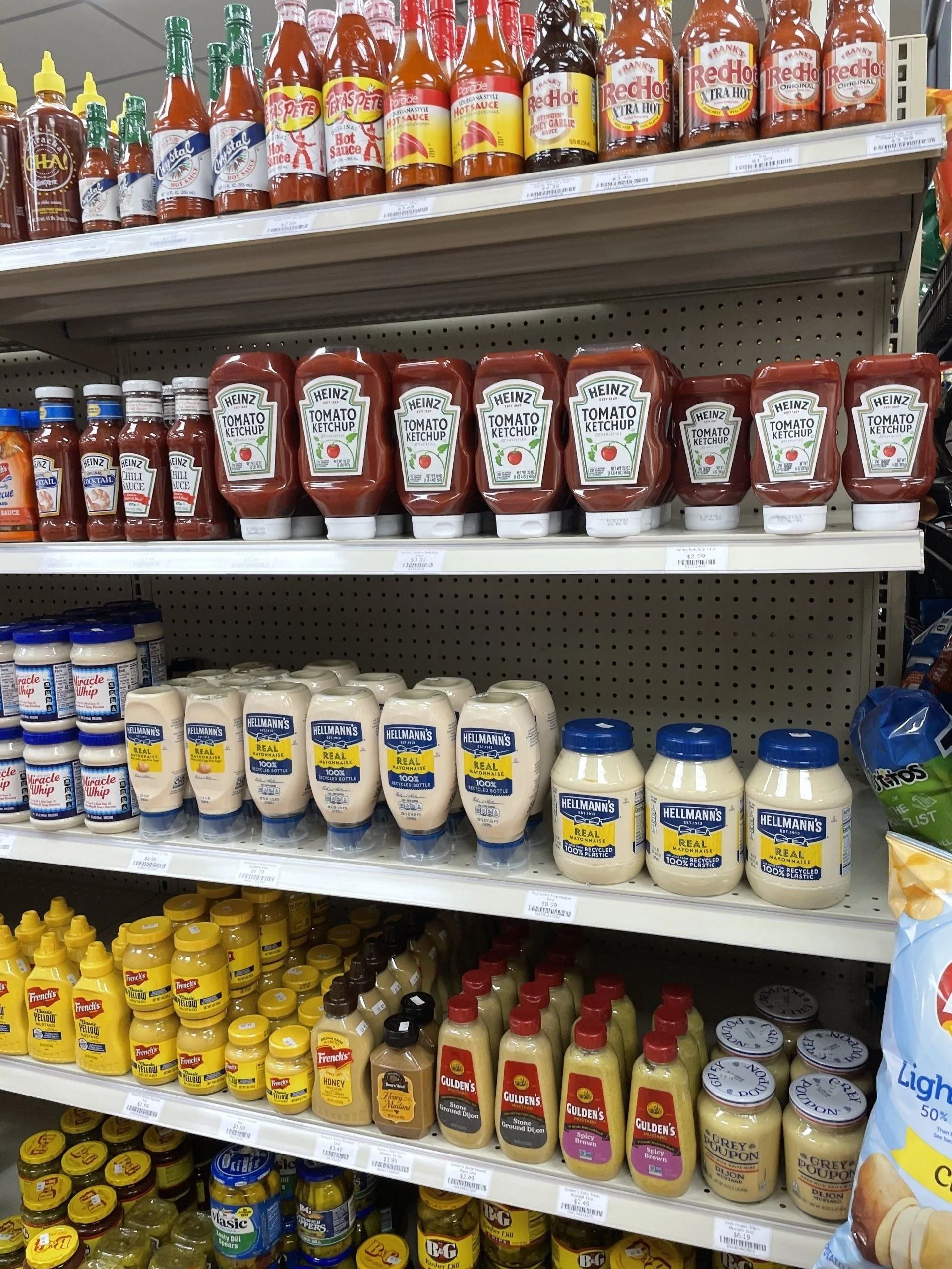 Shelves stocked with various condiment bottles: ketchup, mayonnaise, mustard, and hot sauce.