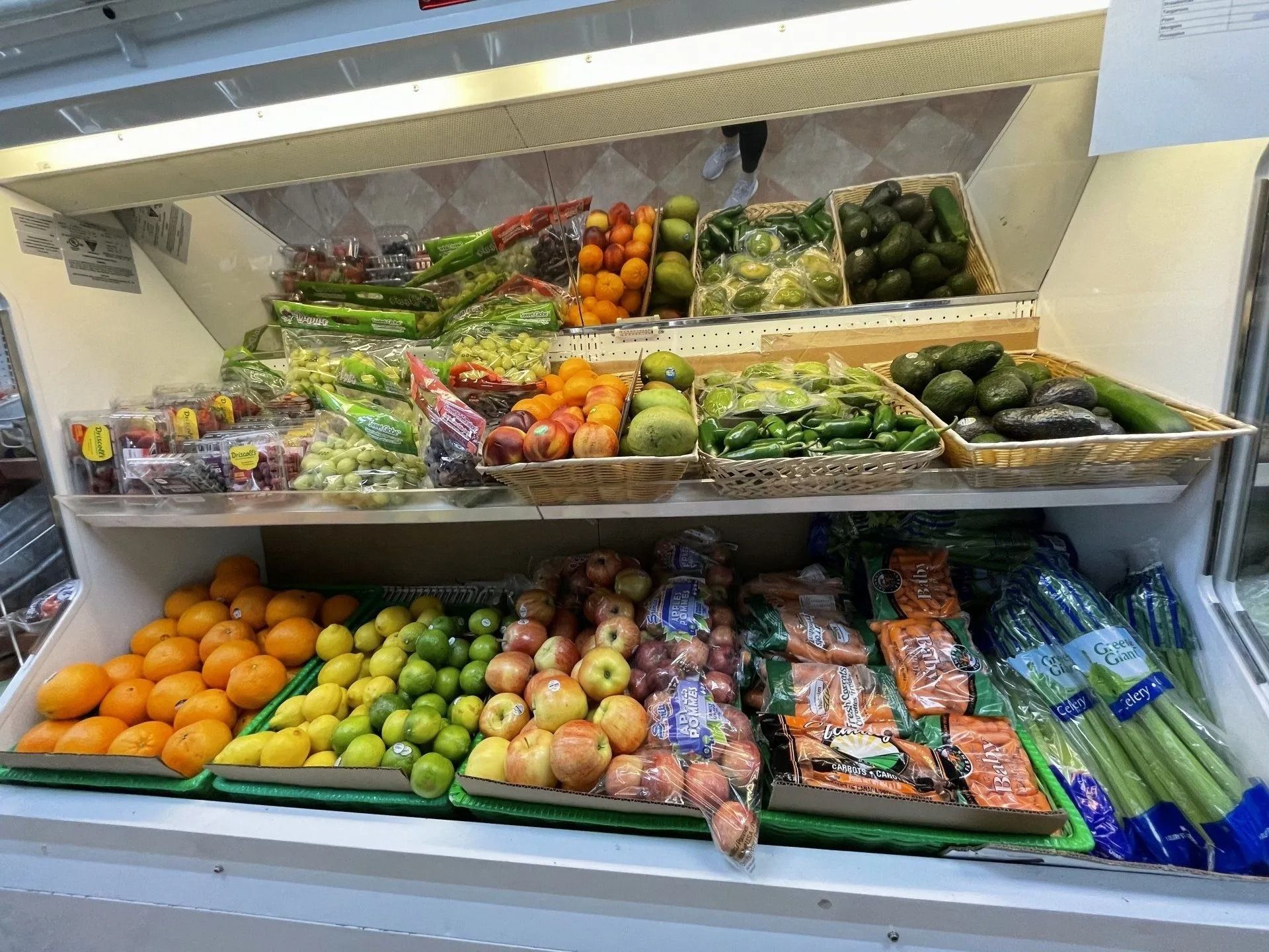 Produce display in a refrigerated case. Features oranges, limes, apples, avocados, celery, grapes, and other fruits and vegetables.