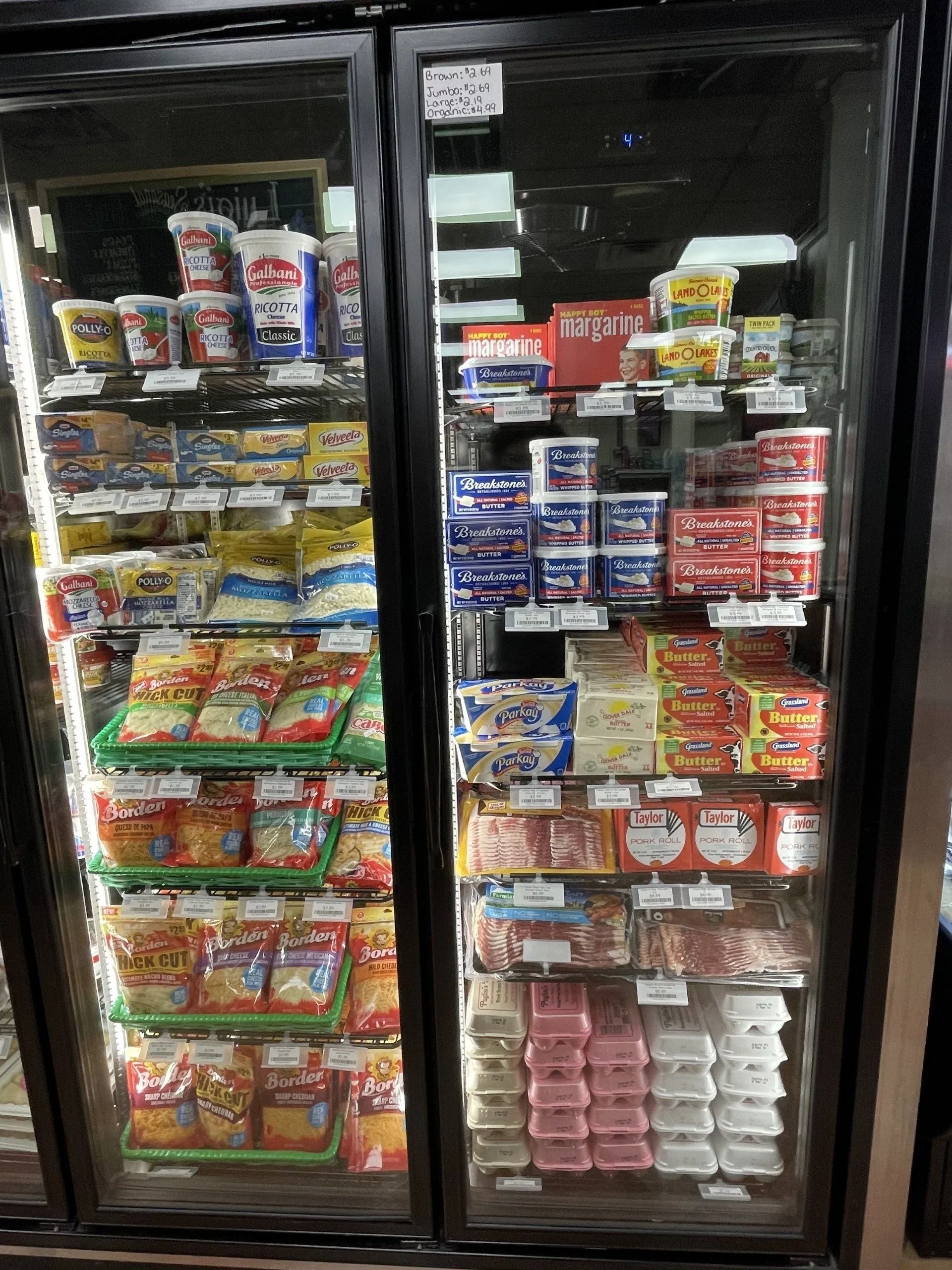 Glass-door refrigerator stocked with dairy products, including butter, yogurt, and cheese, in a store.