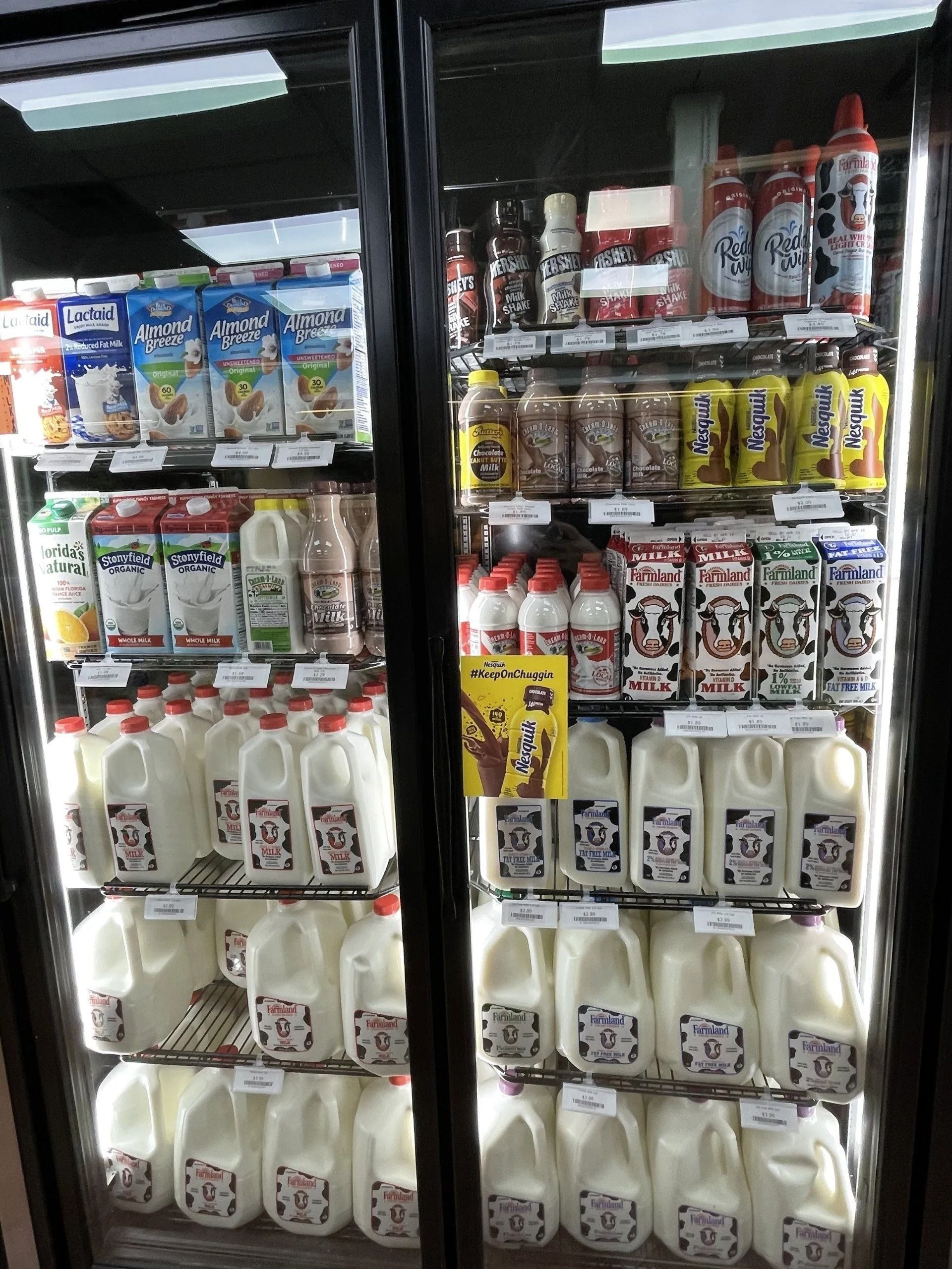 Refrigerator case filled with milk cartons and bottles, including white, chocolate, and other flavored options.