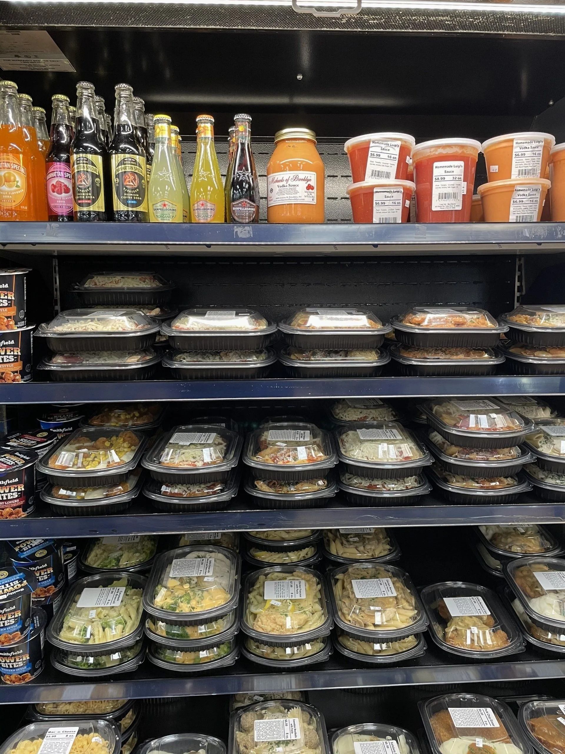 Shelves in a store filled with drinks and prepared food in clear containers.
