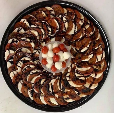 Caprese salad platter: sliced tomatoes and mozzarella, drizzled with balsamic glaze, and a small bowl of cherry tomatoes and mozzarella balls.