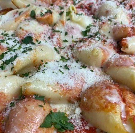Close-up of a cheesy, tomato-sauce-covered pasta dish, sprinkled with herbs and grated cheese.