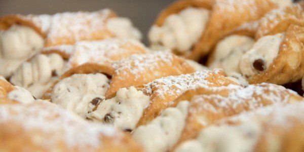 Close-up of cannolis dusted with powdered sugar, filled with cream and chocolate chips.