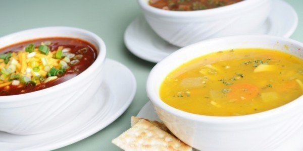 Three bowls of soup on white plates; one chili, one yellow vegetable soup, and one brown soup.
