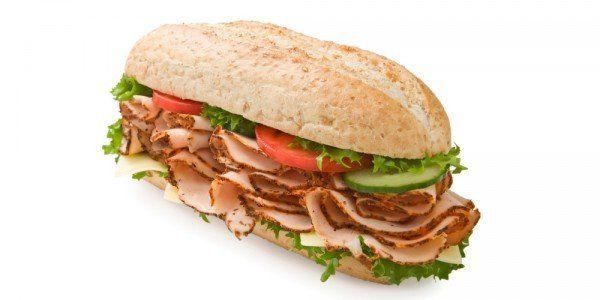 Turkey sandwich with lettuce, tomato, cucumber, and cheese on a sesame seed roll.