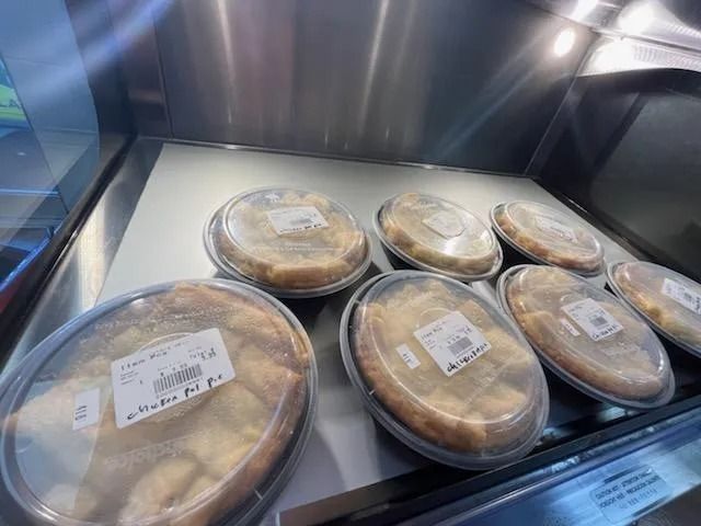 Display case with several pies in clear plastic containers.