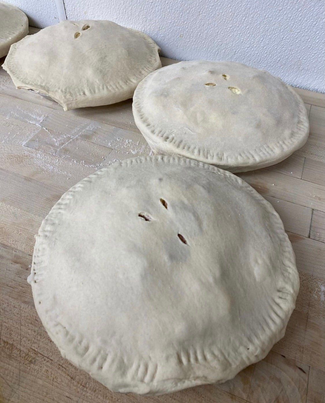 Unbaked, round hand pies with crimped edges and vent slits on a wooden surface.