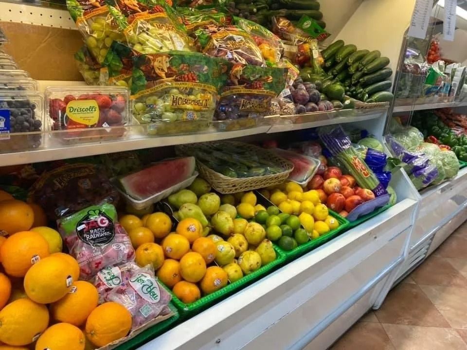 Produce display with oranges, lemons, tomatoes, watermelon, and packaged greens.