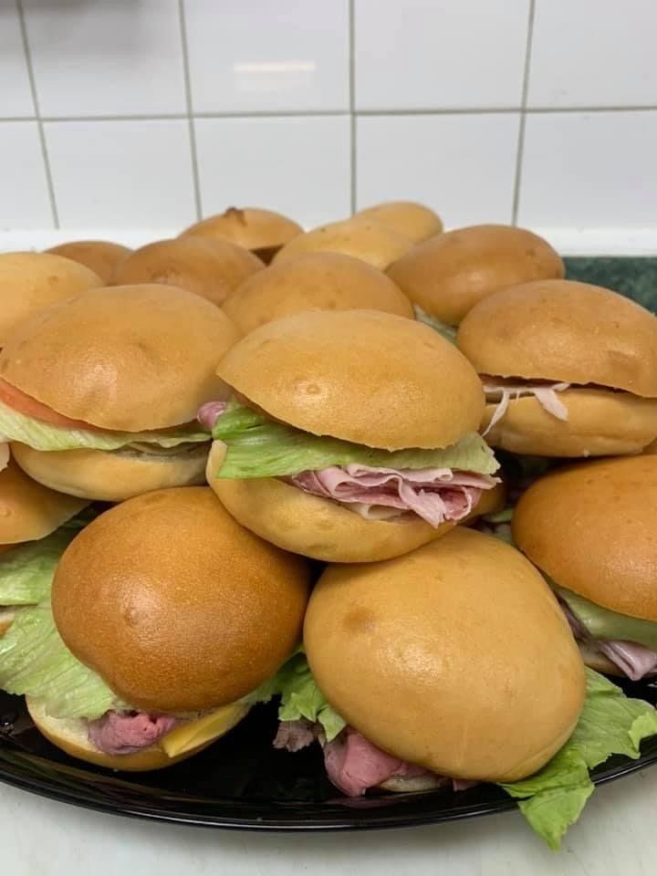 A black platter piled with various sandwich sliders on golden buns, featuring lettuce, meat, and cheese.