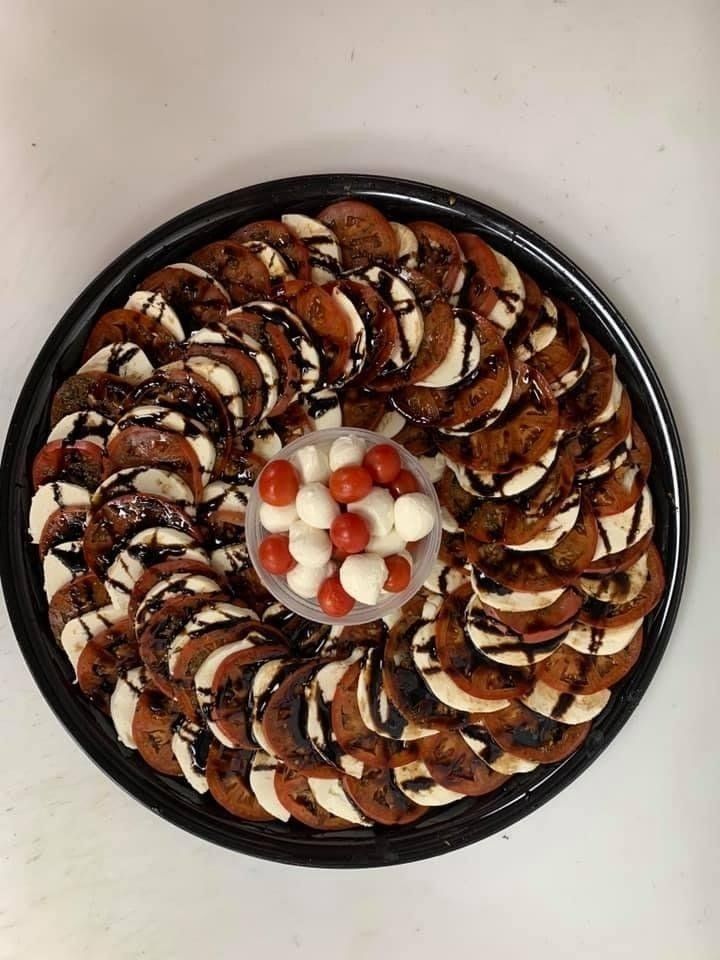 Caprese salad platter: tomato and mozzarella slices drizzled with balsamic glaze, central container of cherry tomatoes and mozzarella balls.