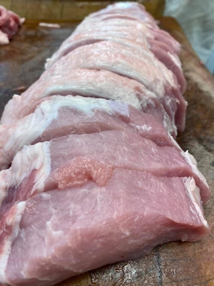 Sliced raw pork loin on a wooden cutting board, ready for cooking. Pink meat, white fat.