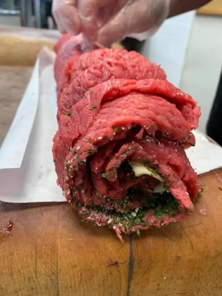 Beef roulade being tied with string on a wooden cutting board, ready for cooking.