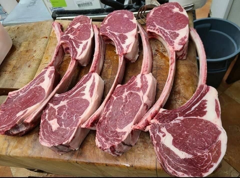 Tomahawk steaks arranged on a wooden butcher block; red meat with visible marbling and long bone handles.