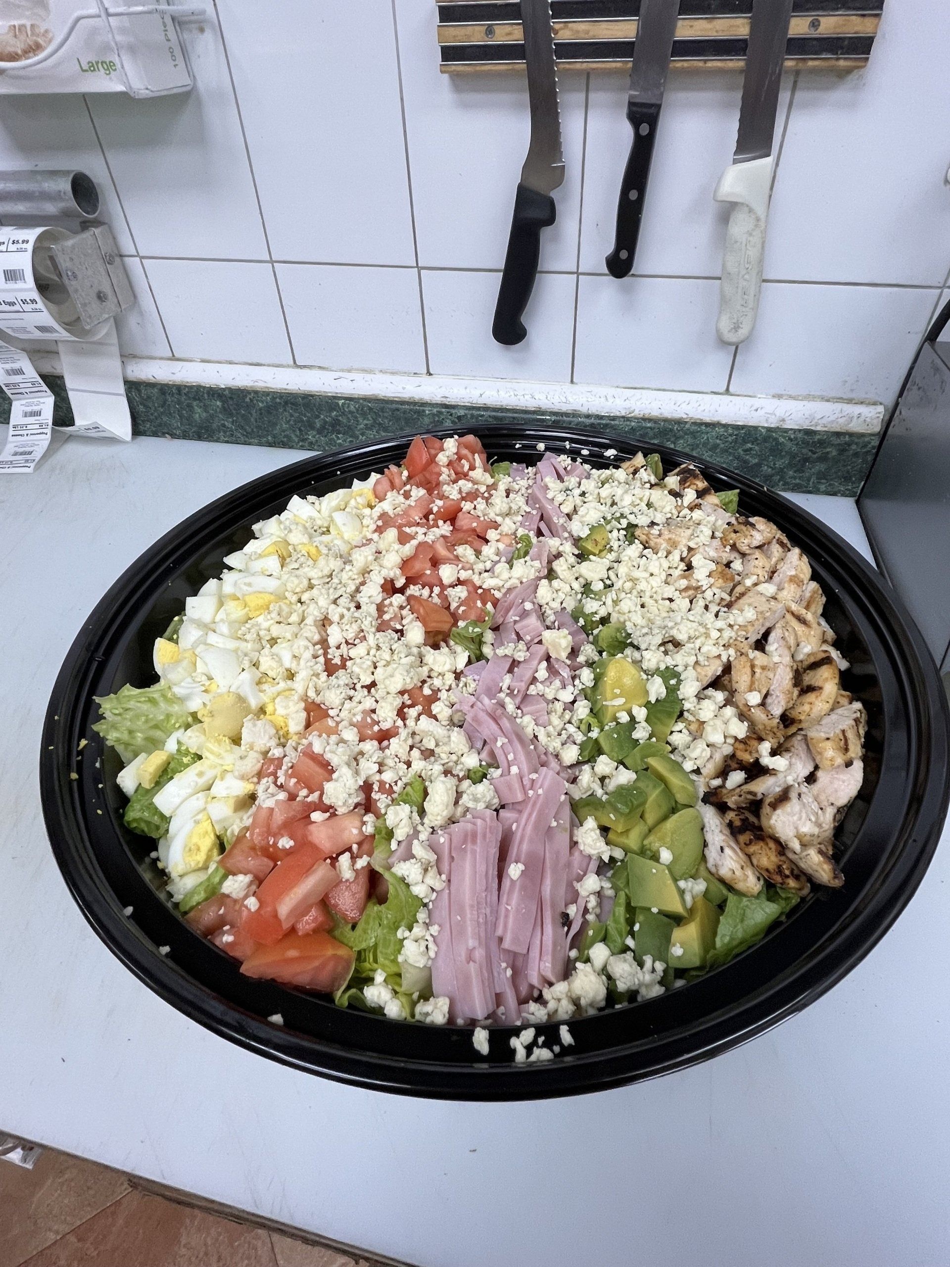 Large salad in a black bowl, with various toppings, including chicken, tomatoes, and cheese.