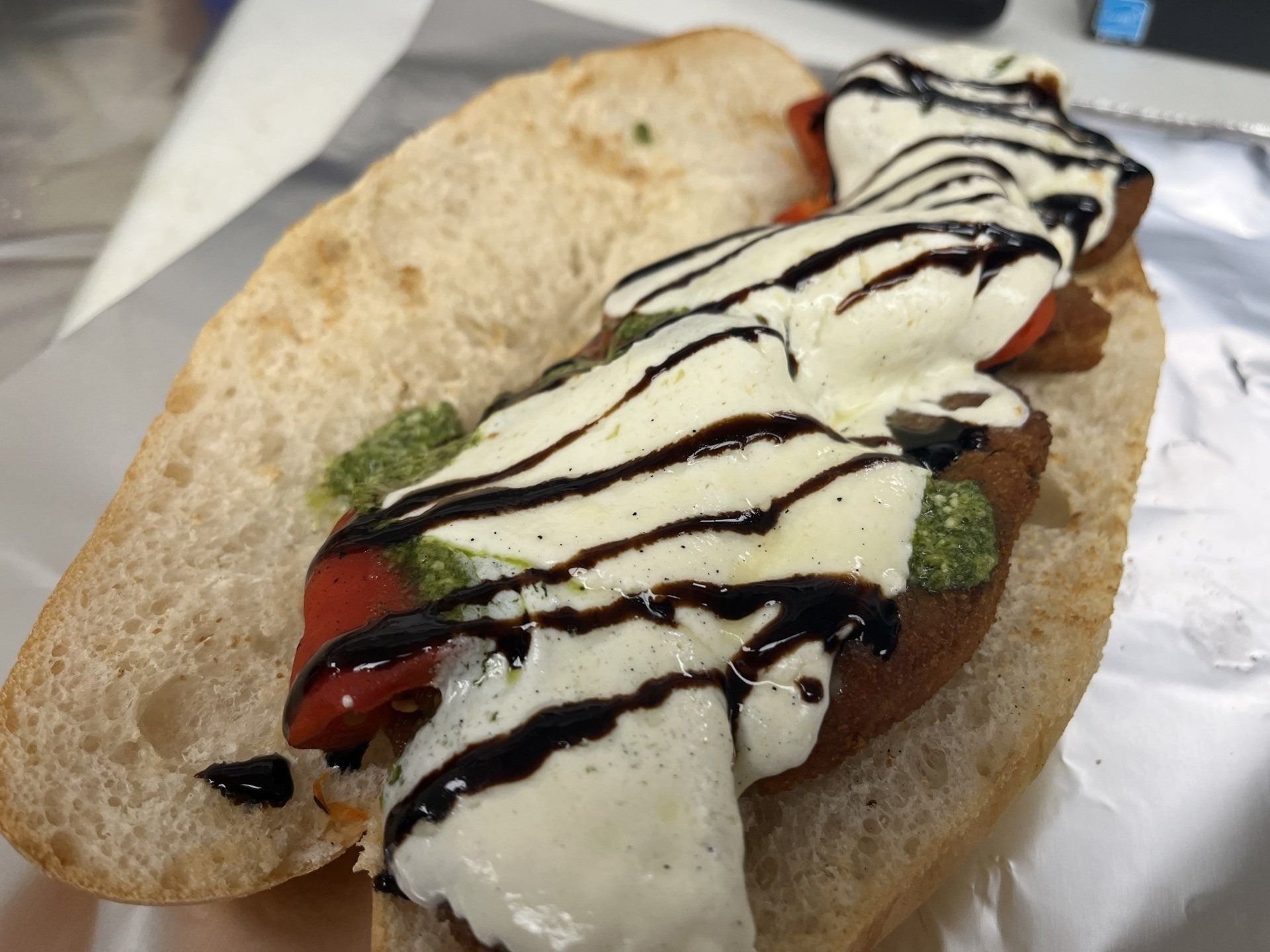 Sub sandwich with pesto, tomatoes, mozzarella, and balsamic glaze on foil.
