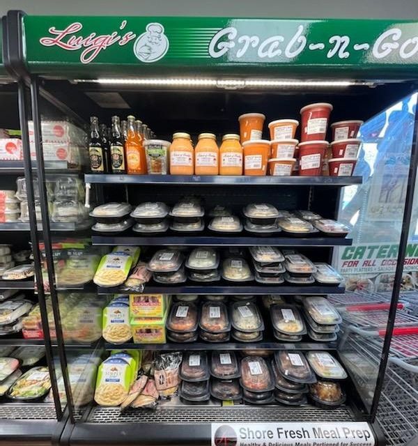A refrigerator at Luigi's Grab-n-Go with various prepared foods in containers, including sauces and entrees.
