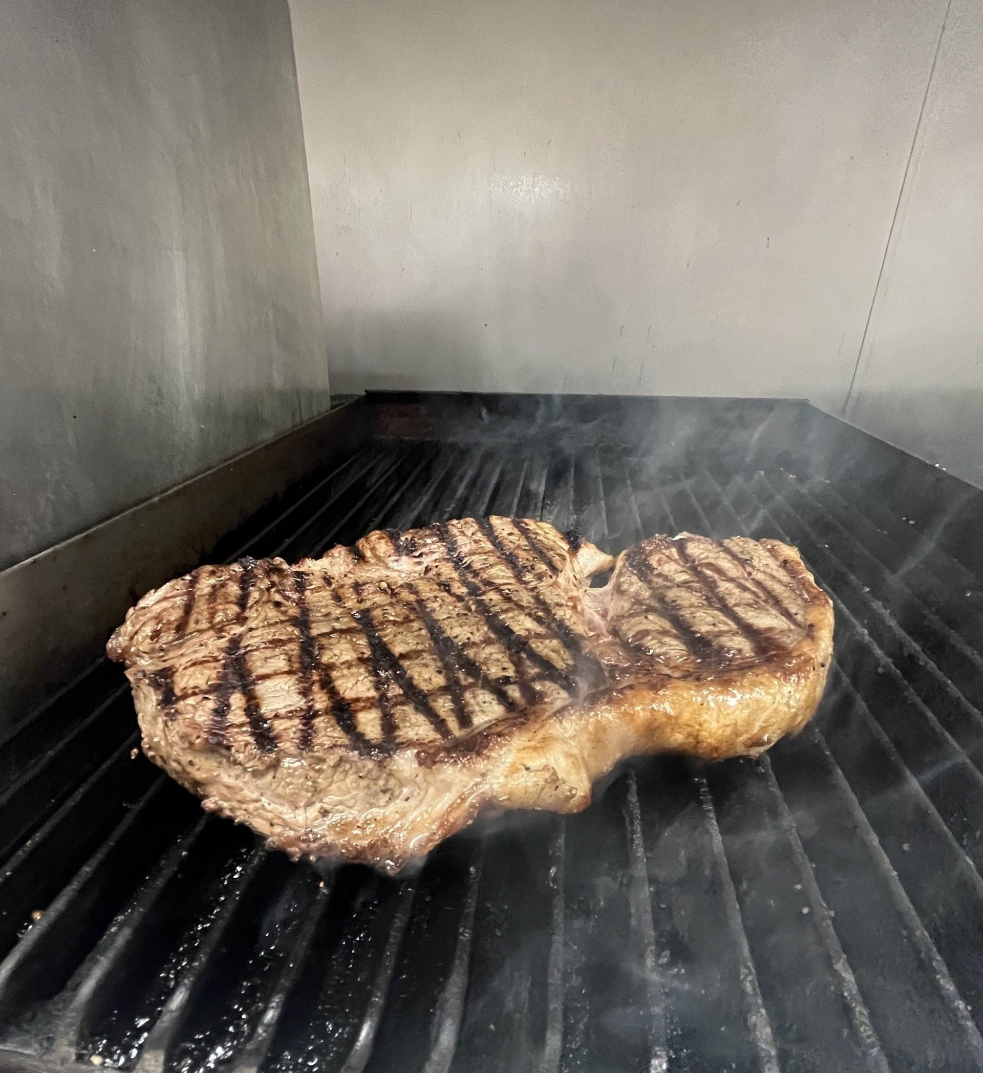 Steak cooking on a grill, with visible grill marks and steam.