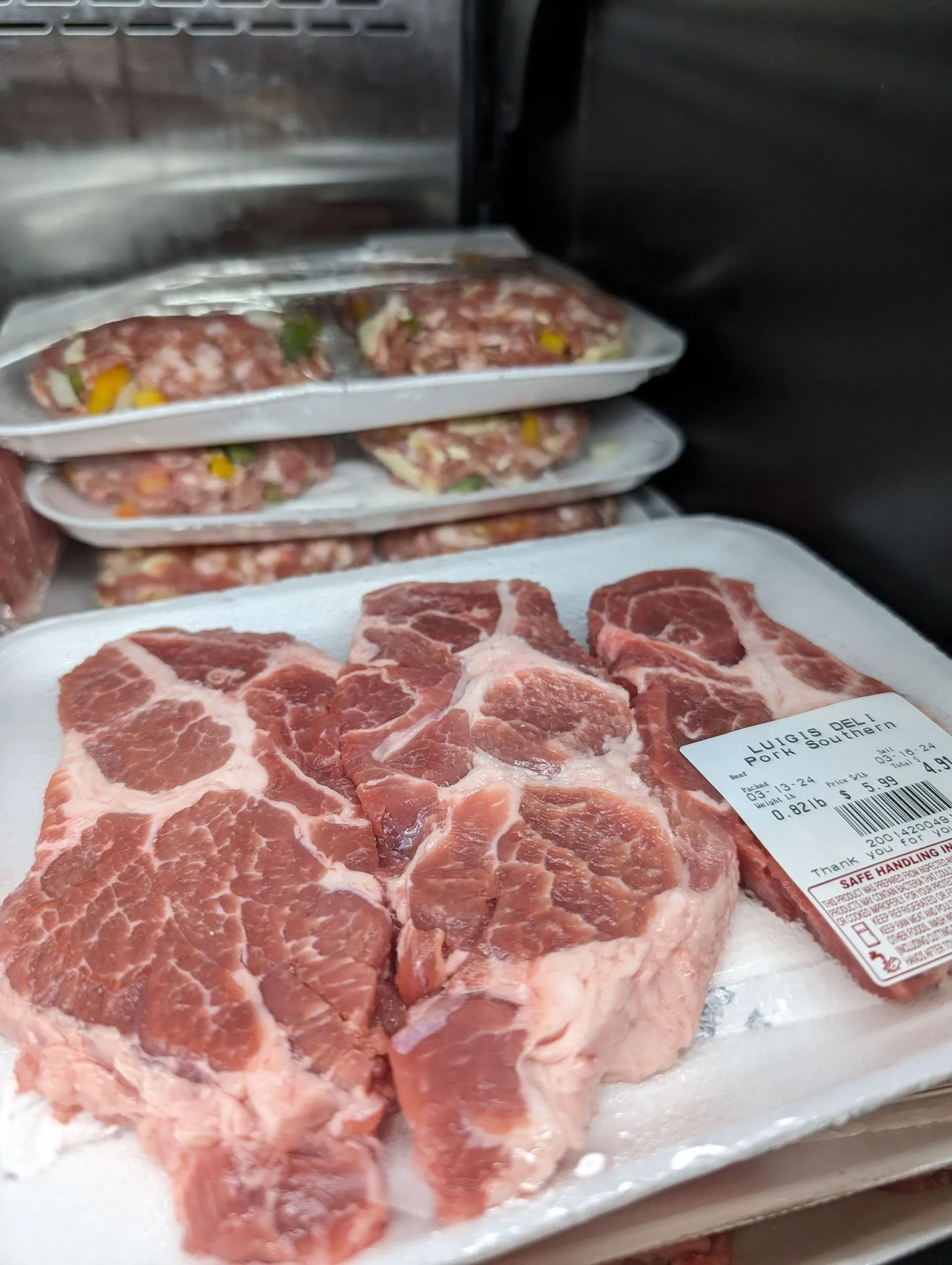 Meat products in a refrigerated display case: pork steaks and sausage patties.
