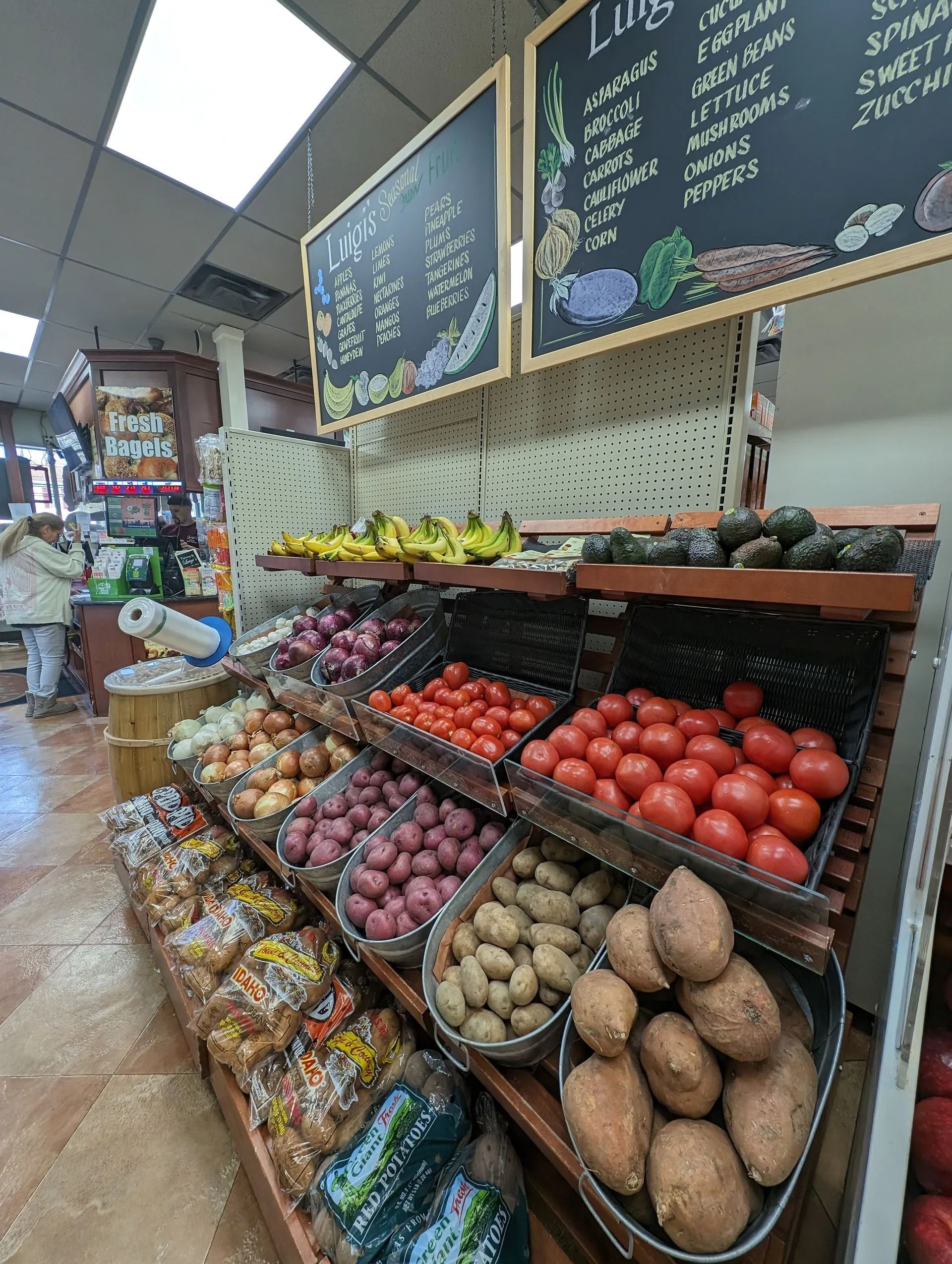 Produce display: tomatoes, onions, potatoes, bananas. Chalkboard menus above.