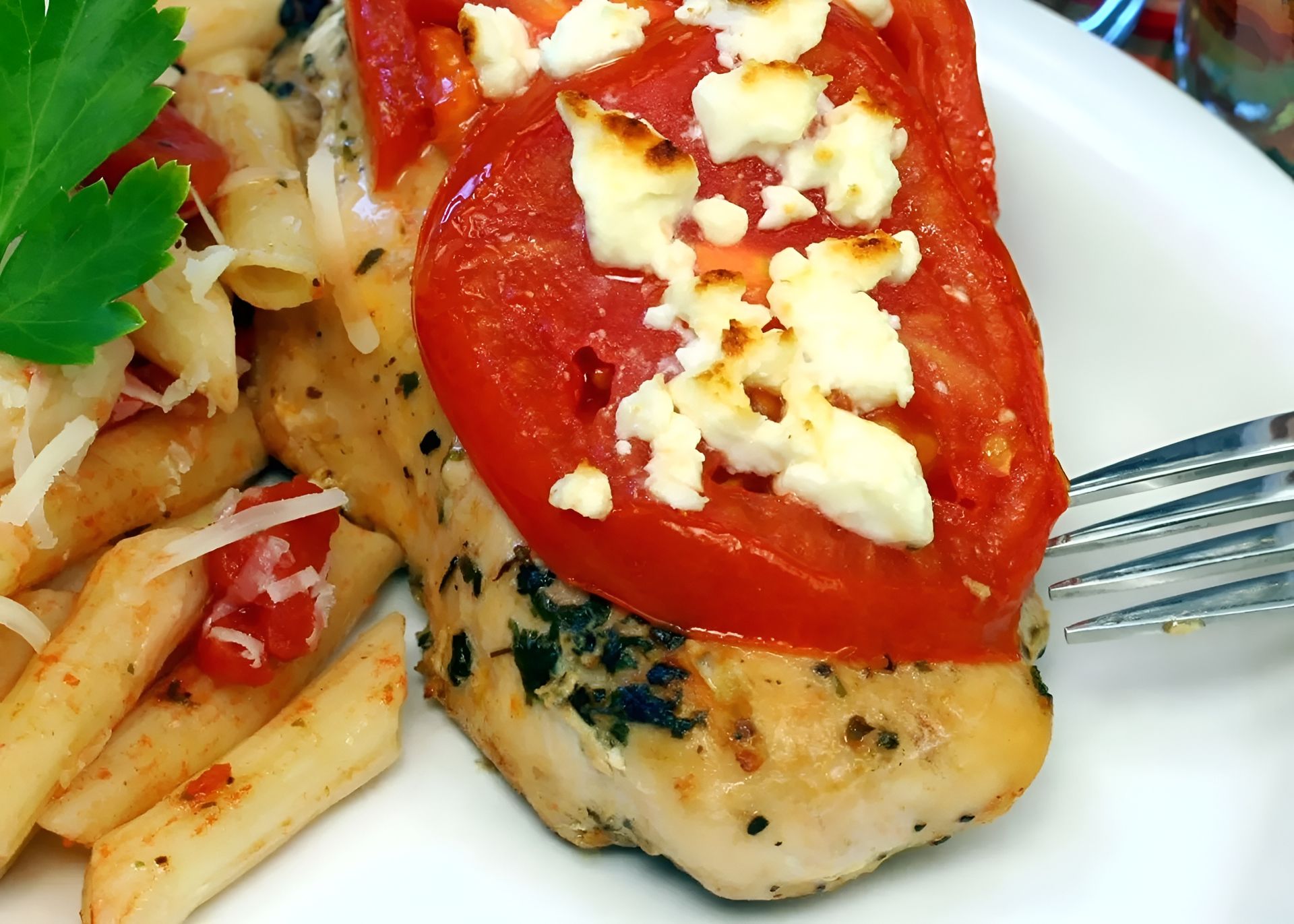 Chicken breast topped with tomato and feta, served with pasta.