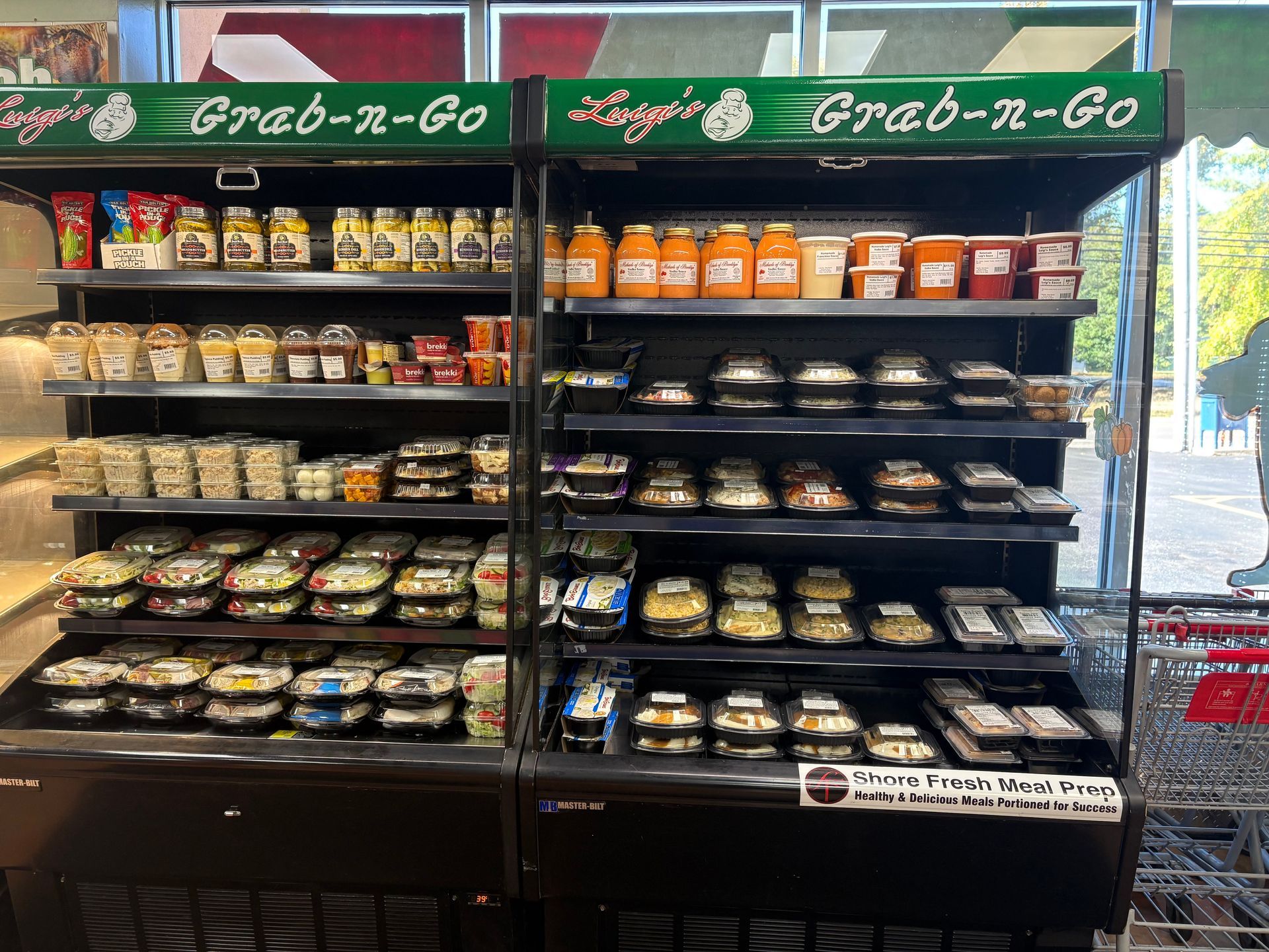 A refrigerated display case at Luigi's Grab-n-Go. Various prepared foods, sauces, and drinks are arranged on shelves.