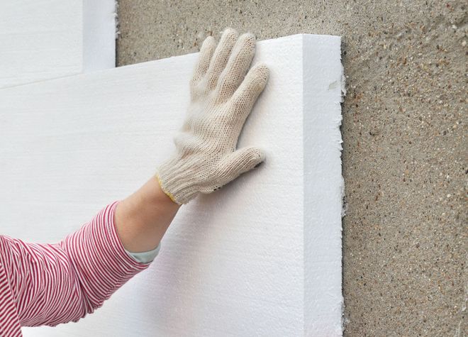 Hand in work glove touching white foam insulation board on a concrete wall