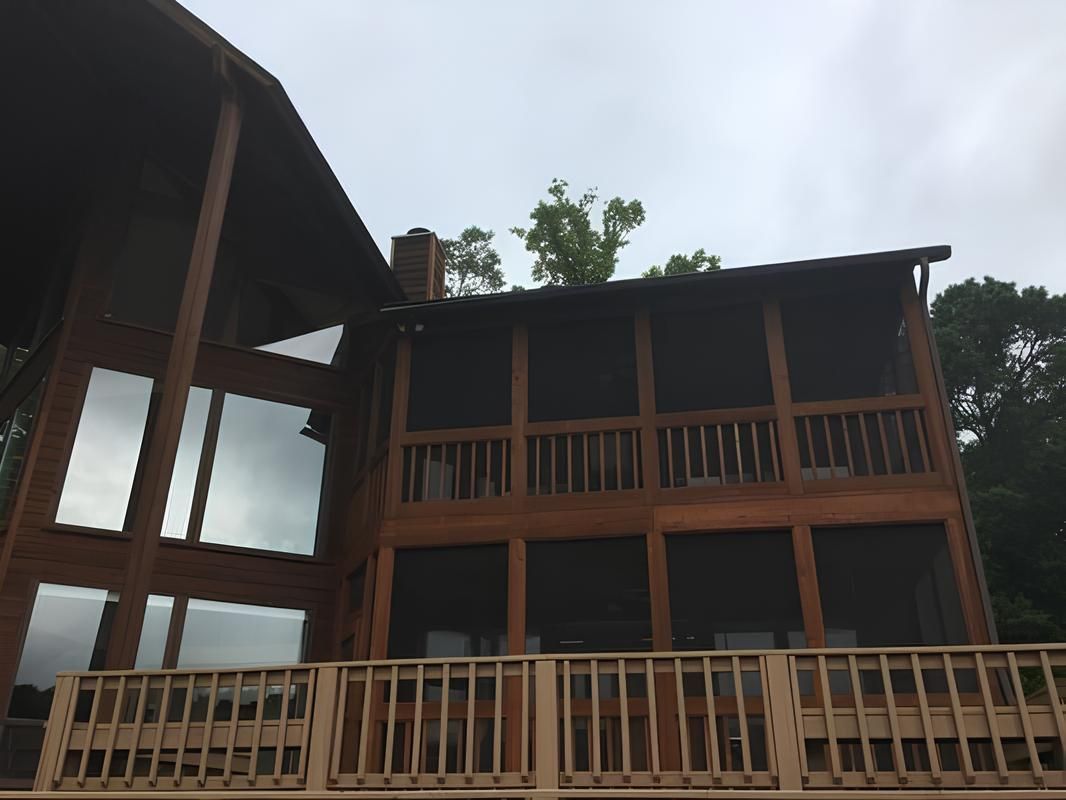 Wooden house with tall windows and a screened porch, overlooking a deck. Cloudy sky.