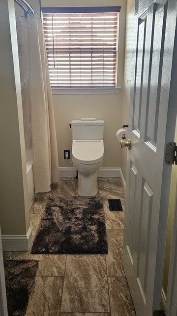 A bathroom with a toilet , shower , and window.