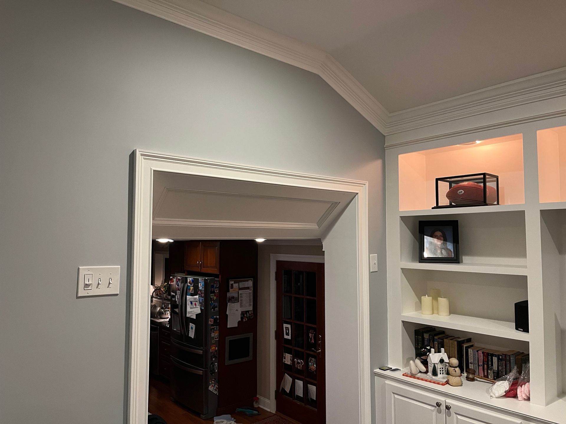 A living room with a built in bookshelf and a doorway leading to a kitchen.