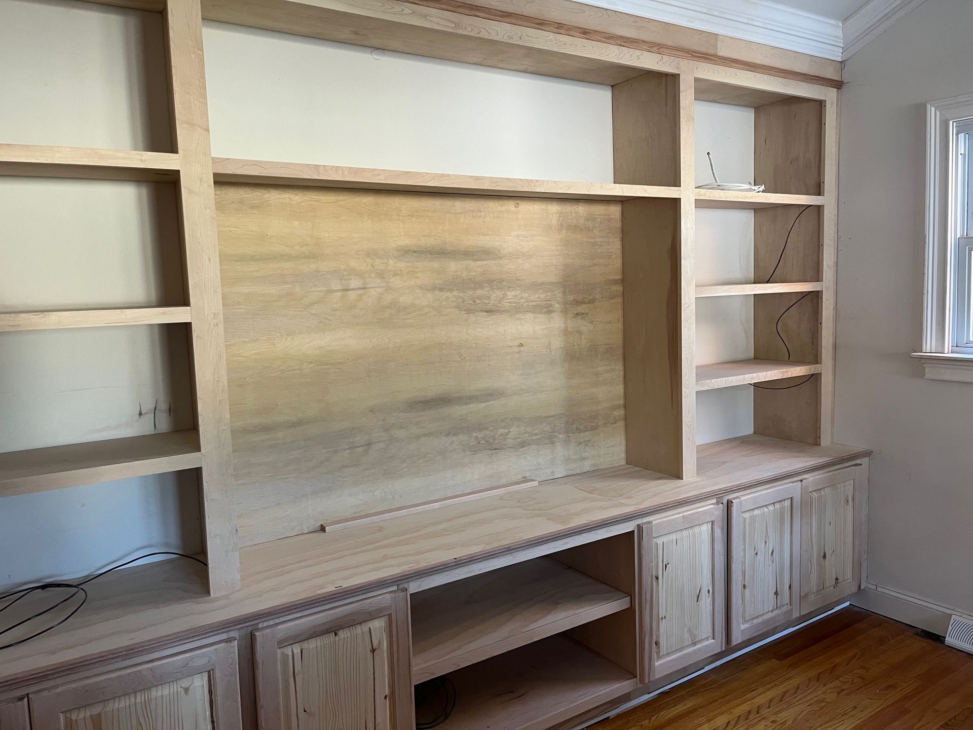 A wooden entertainment center is being built in a room with a window.