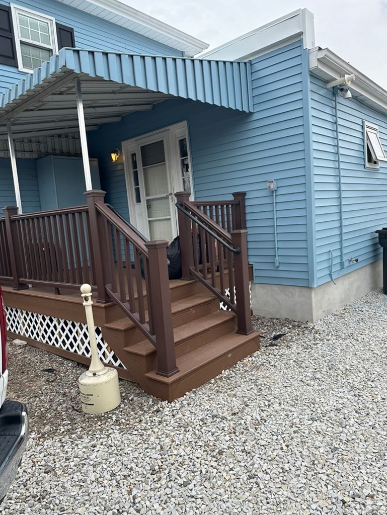 A blue mobile home with a wooden deck and stairs.