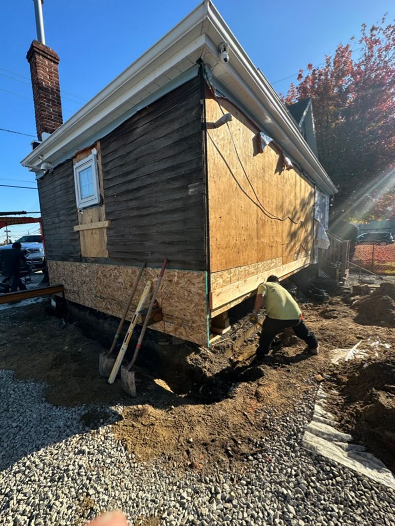 A man is digging a hole in front of a house that is being moved.