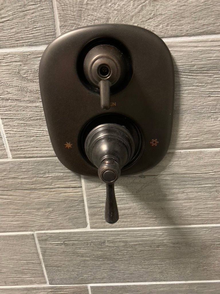 A close up of a shower faucet on a tiled wall.