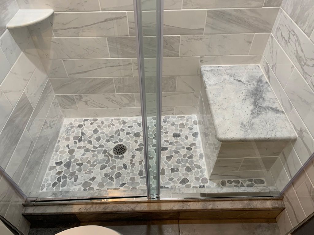A bathroom with a walk in shower and a marble bench.