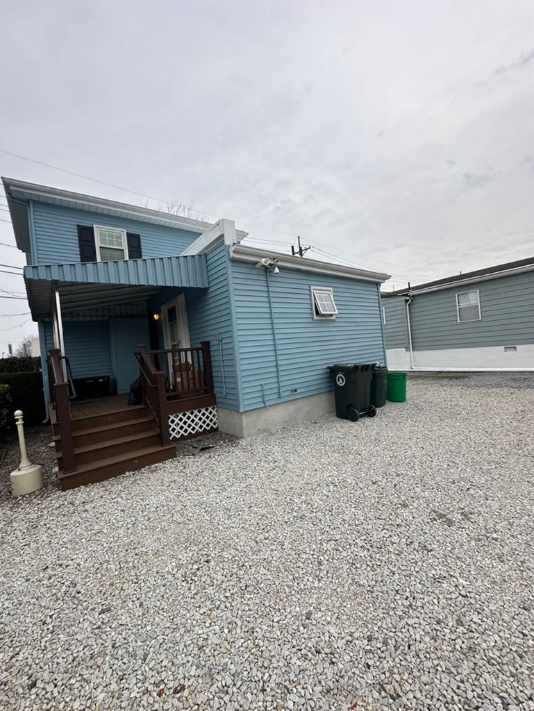 A blue mobile home with a porch and stairs in a gravel lot.