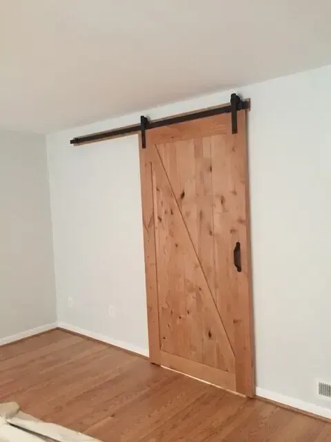 A wooden sliding barn door is in a room with hardwood floors.