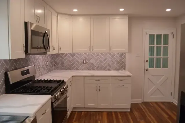 A kitchen with white cabinets , a stove , a microwave and a door.