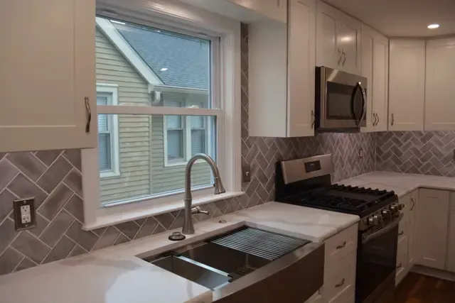 A kitchen with a sink , stove , microwave and window.