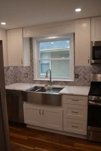 A kitchen with white cabinets , stainless steel appliances , a sink and a window.