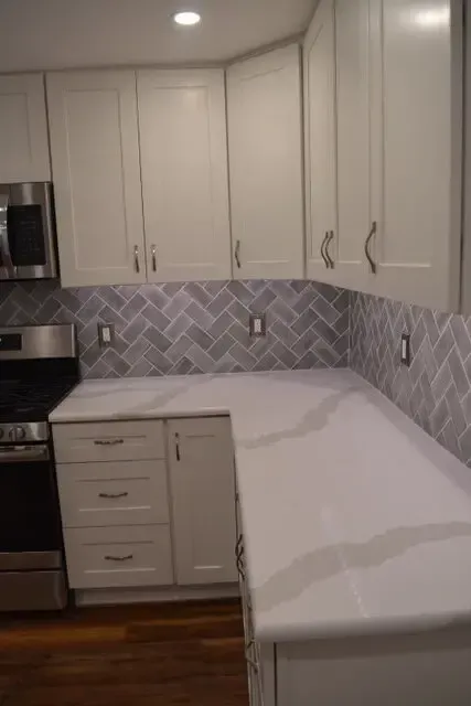 A kitchen with white cabinets , a stove , a microwave , and a counter top.