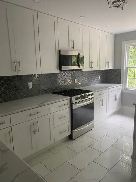 A kitchen with white cabinets , a stove , and a microwave.