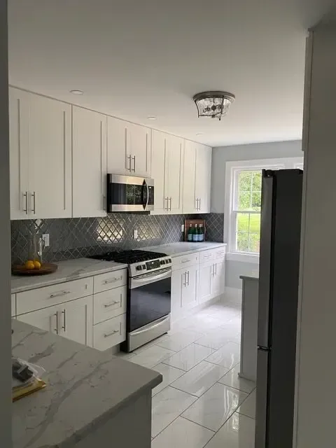 A kitchen with white cabinets , a stove , a refrigerator , and a microwave.