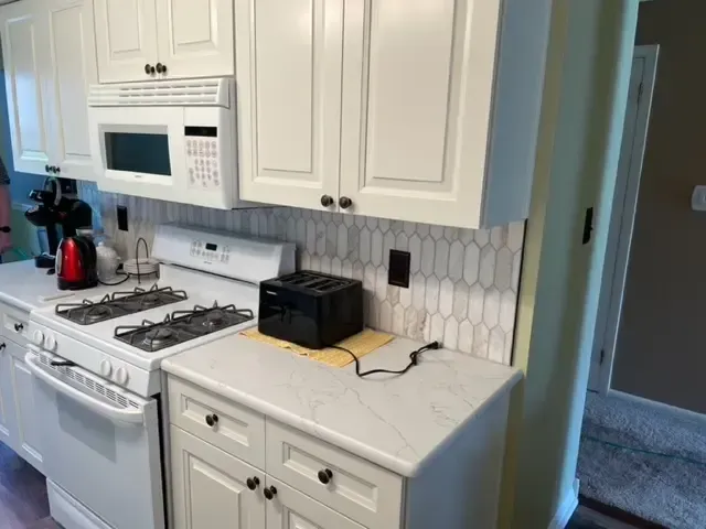 A kitchen with white cabinets , a stove , a microwave , and a toaster oven.