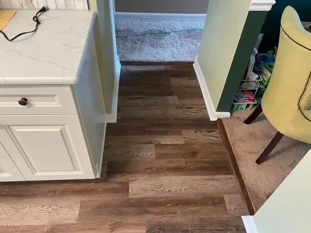 A kitchen with hardwood floors , white cabinets , and a yellow chair.