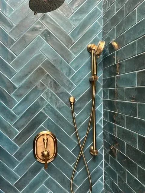A shower with blue tiles and a brass shower head.