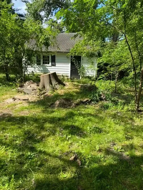 A small white house is surrounded by trees and grass.