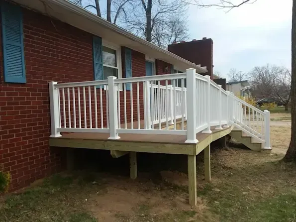 A wooden deck with a white railing is in front of a brick house.