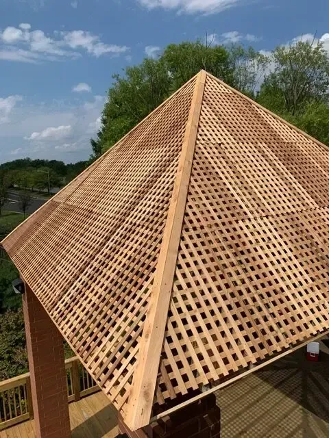 A wooden gazebo with a lattice roof is sitting on top of a wooden deck.