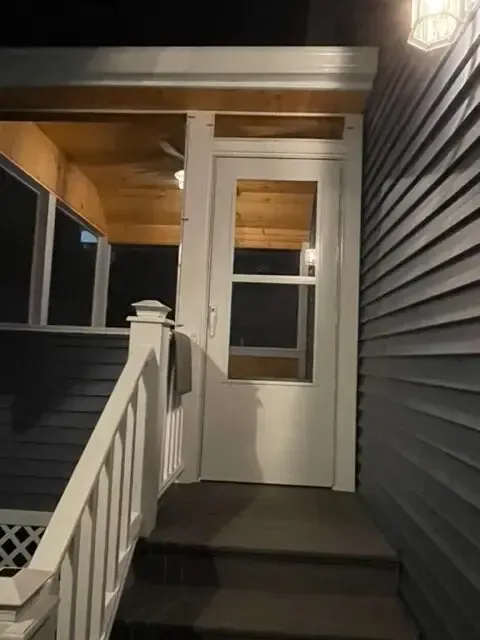 A porch with a white railing and a white door at night.